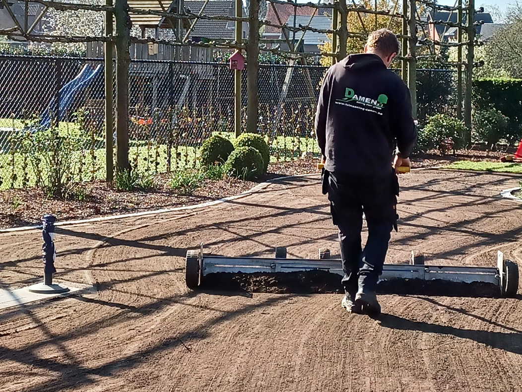 Tuinman aan de slag met egalisatieschuif voor tuinrenovatie in Wuustwezel